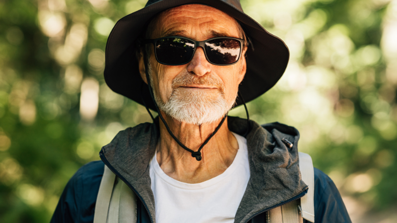 An Elderly Man Hat and Sunglasses Standing Outdoors